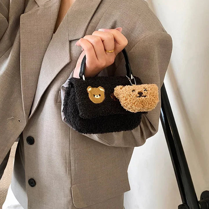Person holding a small black handbag with a Kawaii teddy bear design.