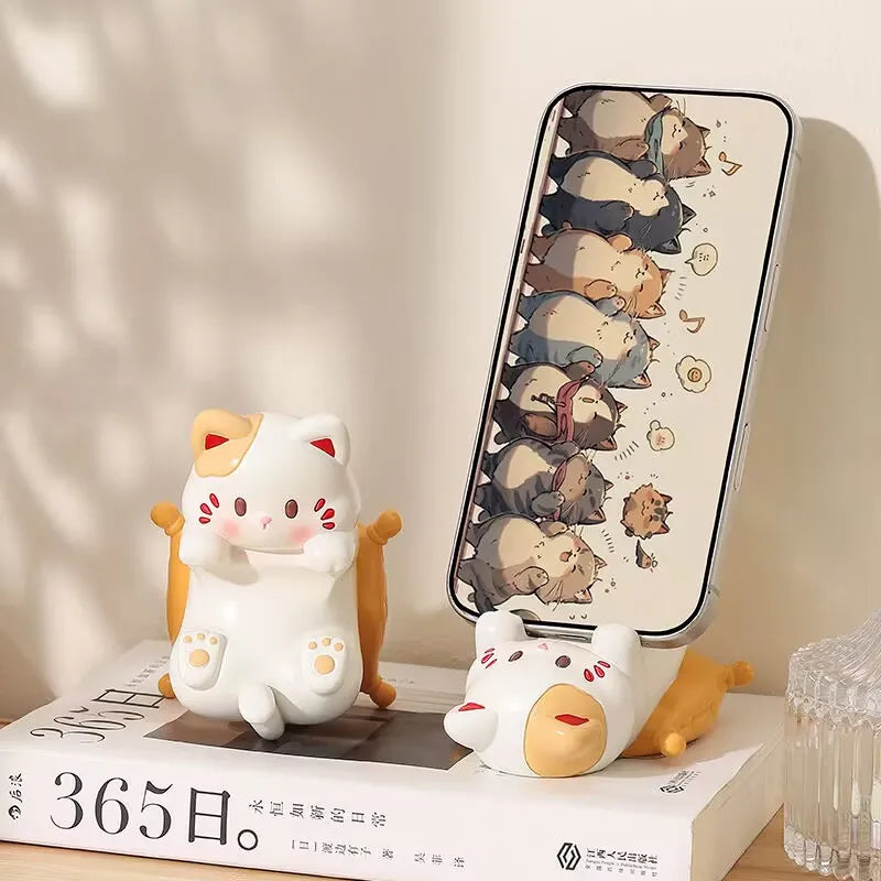 Two kawaii cat-shaped phone stands on a surface with a phone displaying cat illustrations.