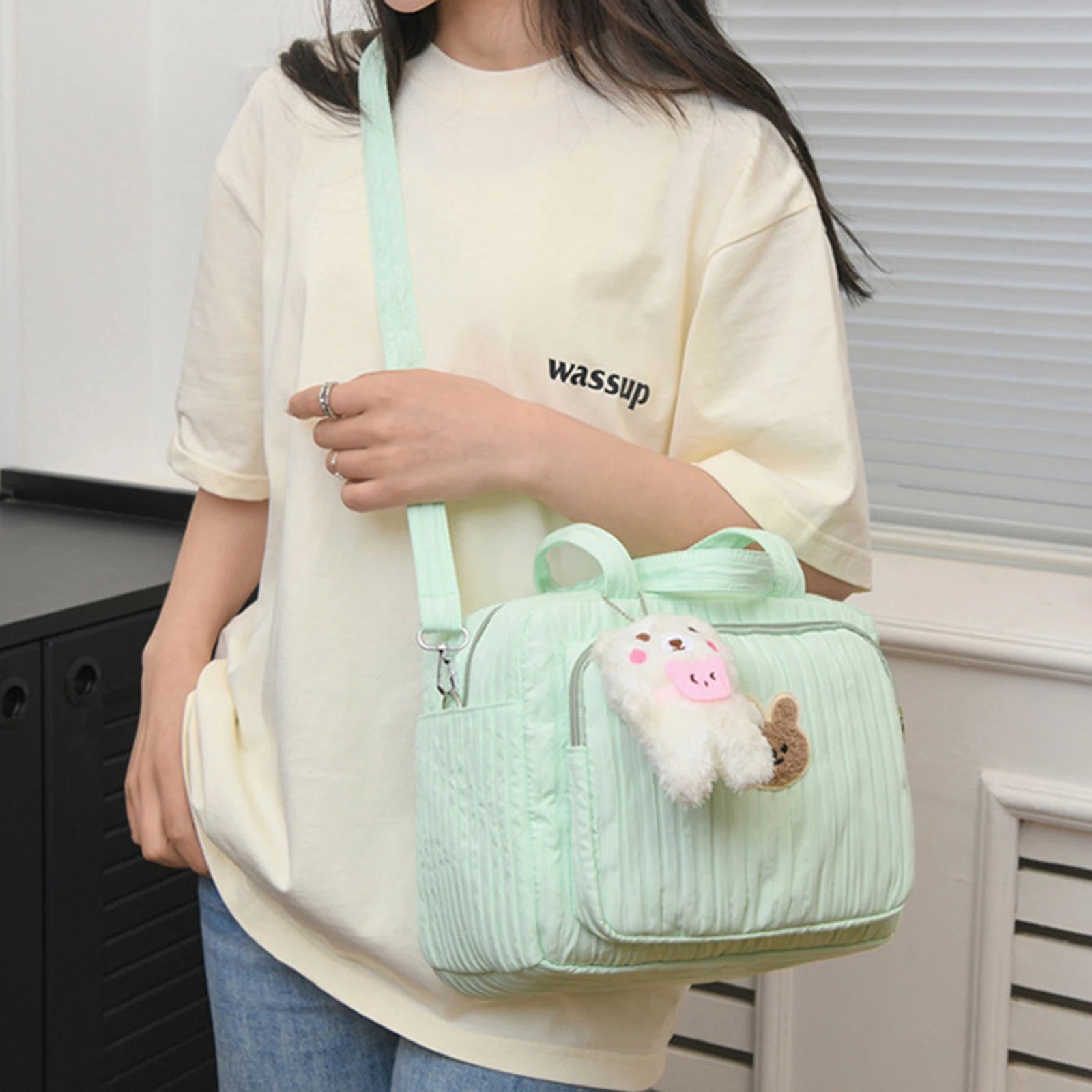 Person holding a light green textured handbag with Kawaii plush toys, wearing a white shirt with 'wassup' text.