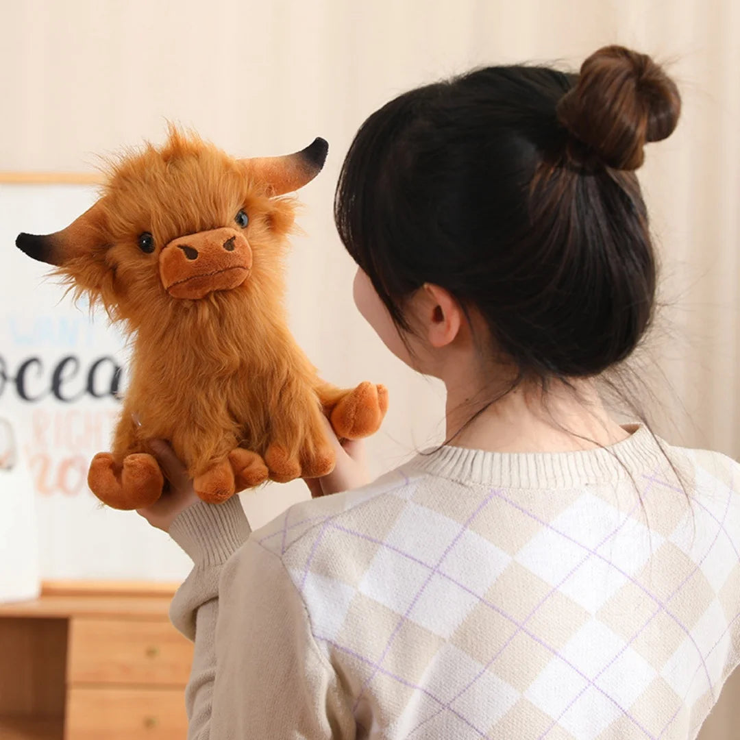 Person holding a kawaii plush Highland cow toy in front of a blurred background