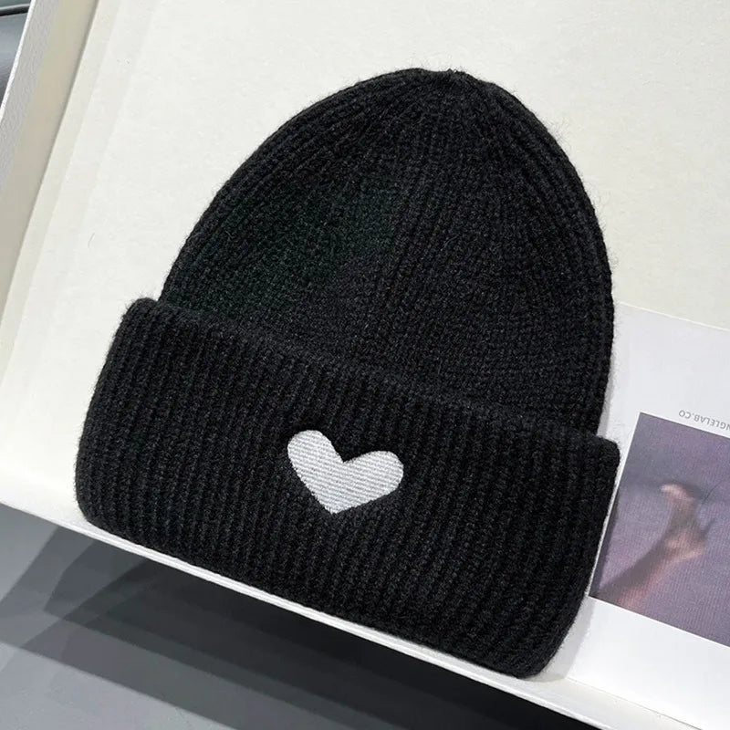 Black knit Kawaii beanie with a white heart on a white surface