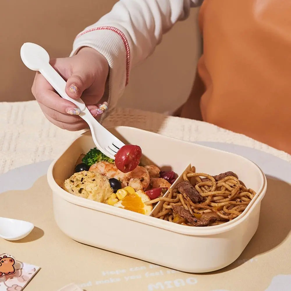 Person holding a fork over a kawaii bento box filled with food on a beige surface.
