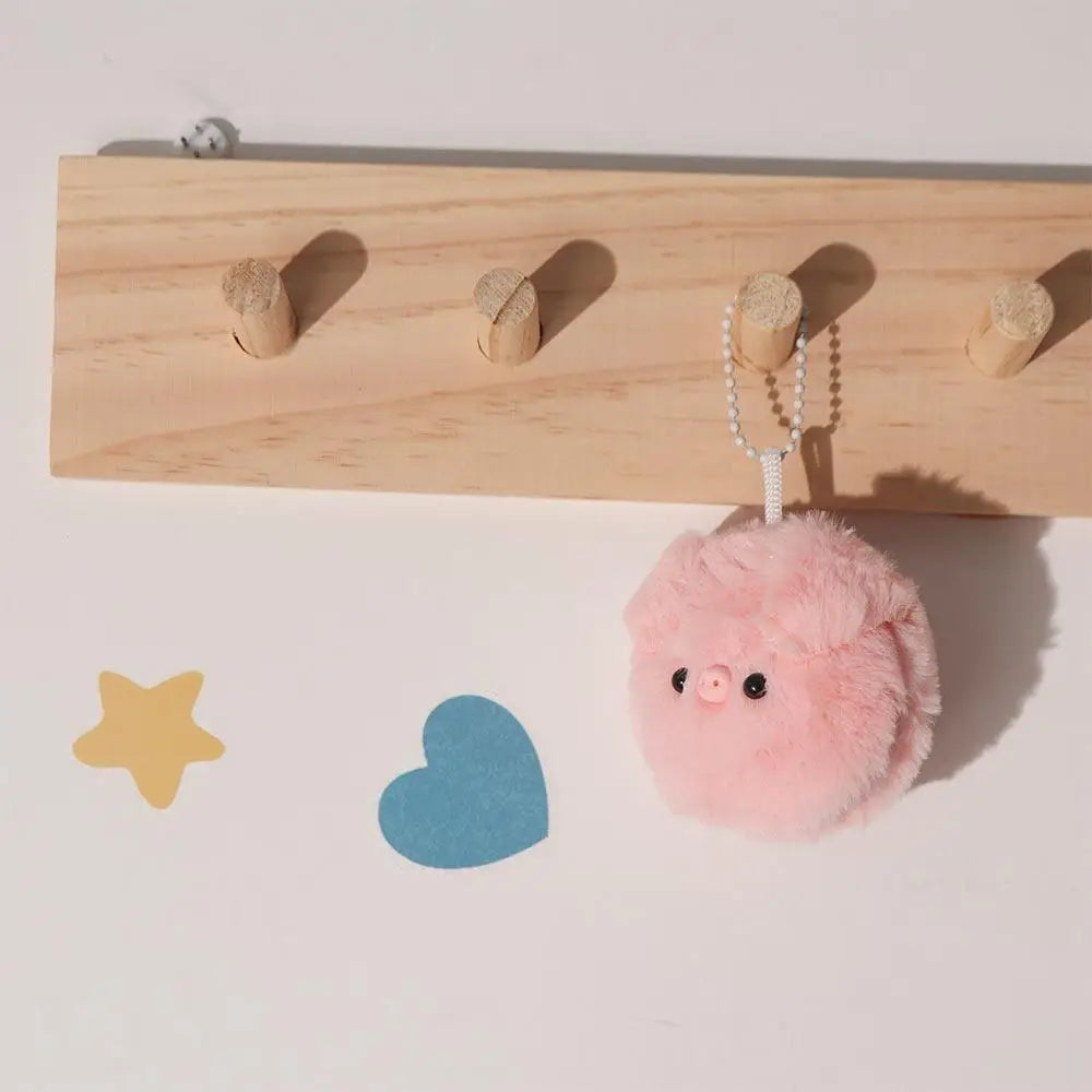 Pink kawaii plush keychain hanging from a wooden pegboard with star and heart decorations on a light background.