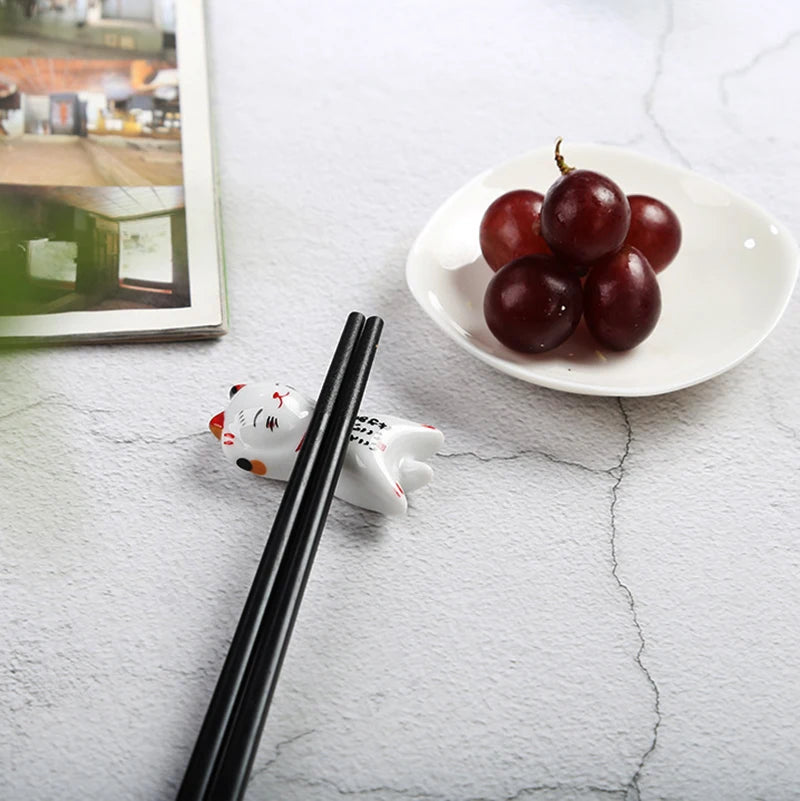Chopsticks on a marble surface with a small kawaii cat-shaped holder and a plate of grapes in the background.