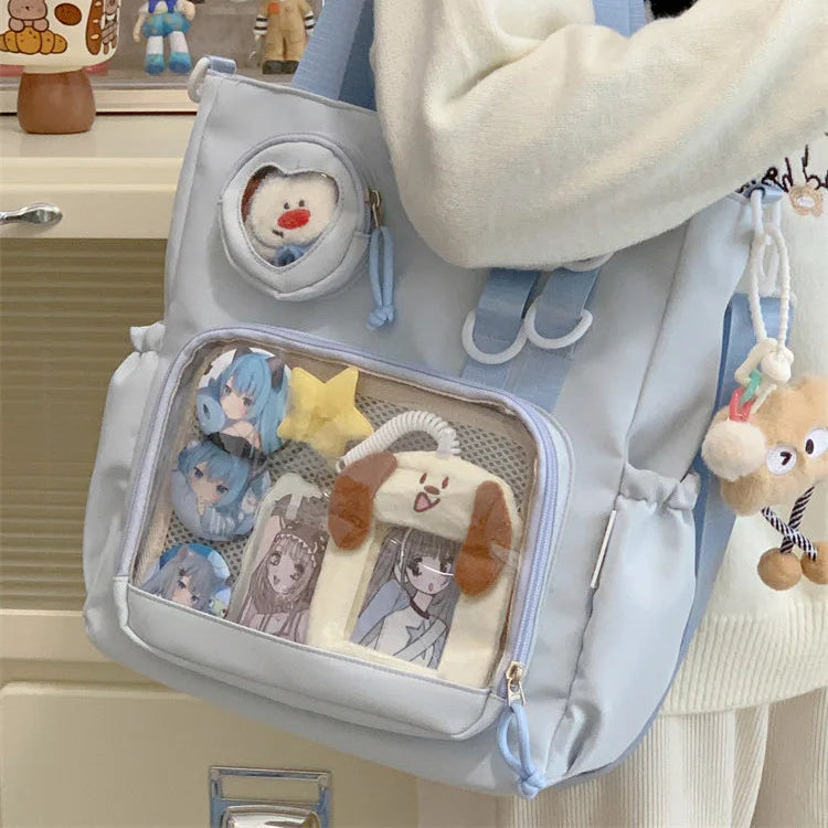 Light blue Kawaii backpack with anime character designs and plush toys, held by a person.