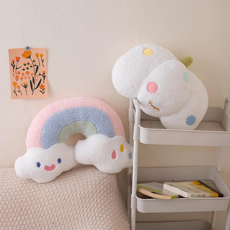 Two cloud-shaped kawaii cushions with rainbow design on a shelf against a light wall.