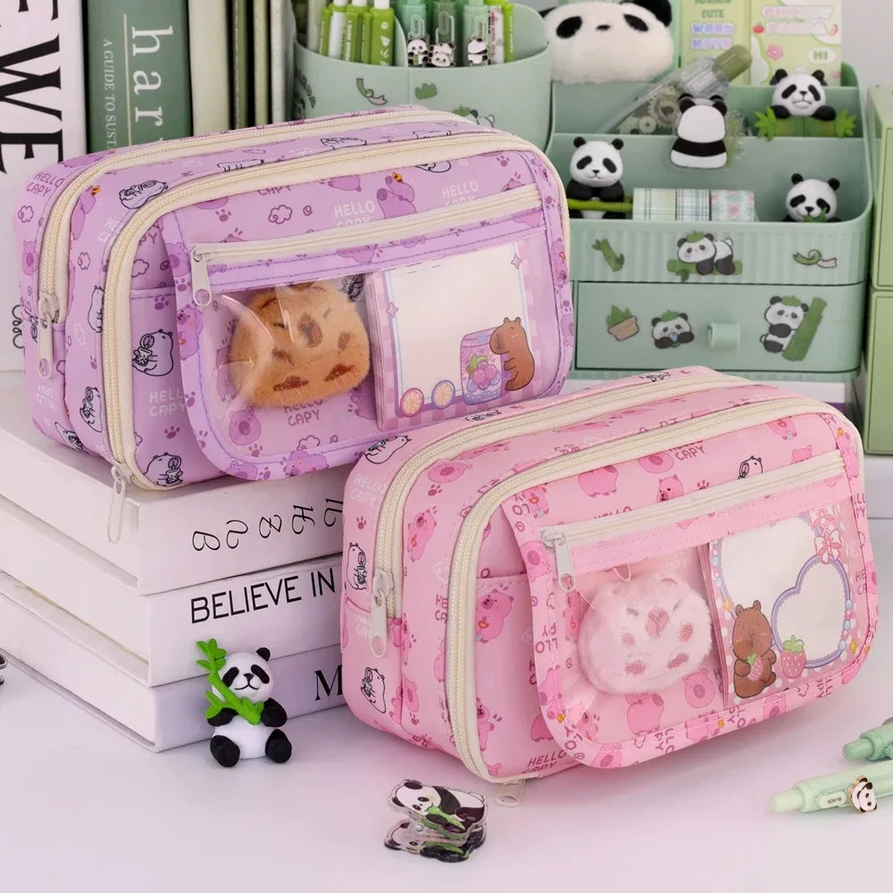 Two pink pencil cases with kawaii cartoon designs on a white surface with books and small panda figurines.
