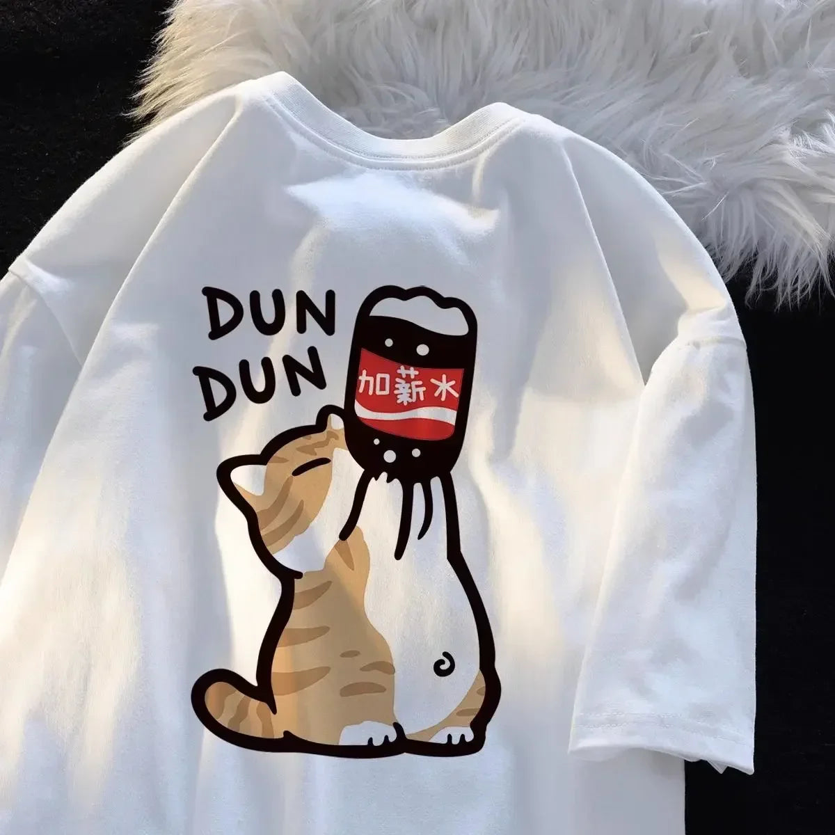 White sweatshirt with kawaii cartoon design of a cat and a bottle labeled 'DUN DUN' on a fluffy white surface.