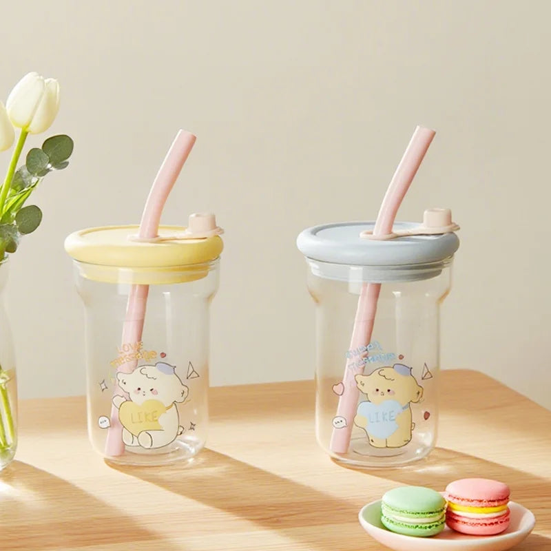 Two clear cups with Kawaii animal illustrations, pink straws, and colorful macarons on a wooden surface.