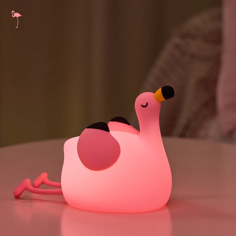 Pink kawaii flamingo-shaped night light on a reflective surface with a blurred background