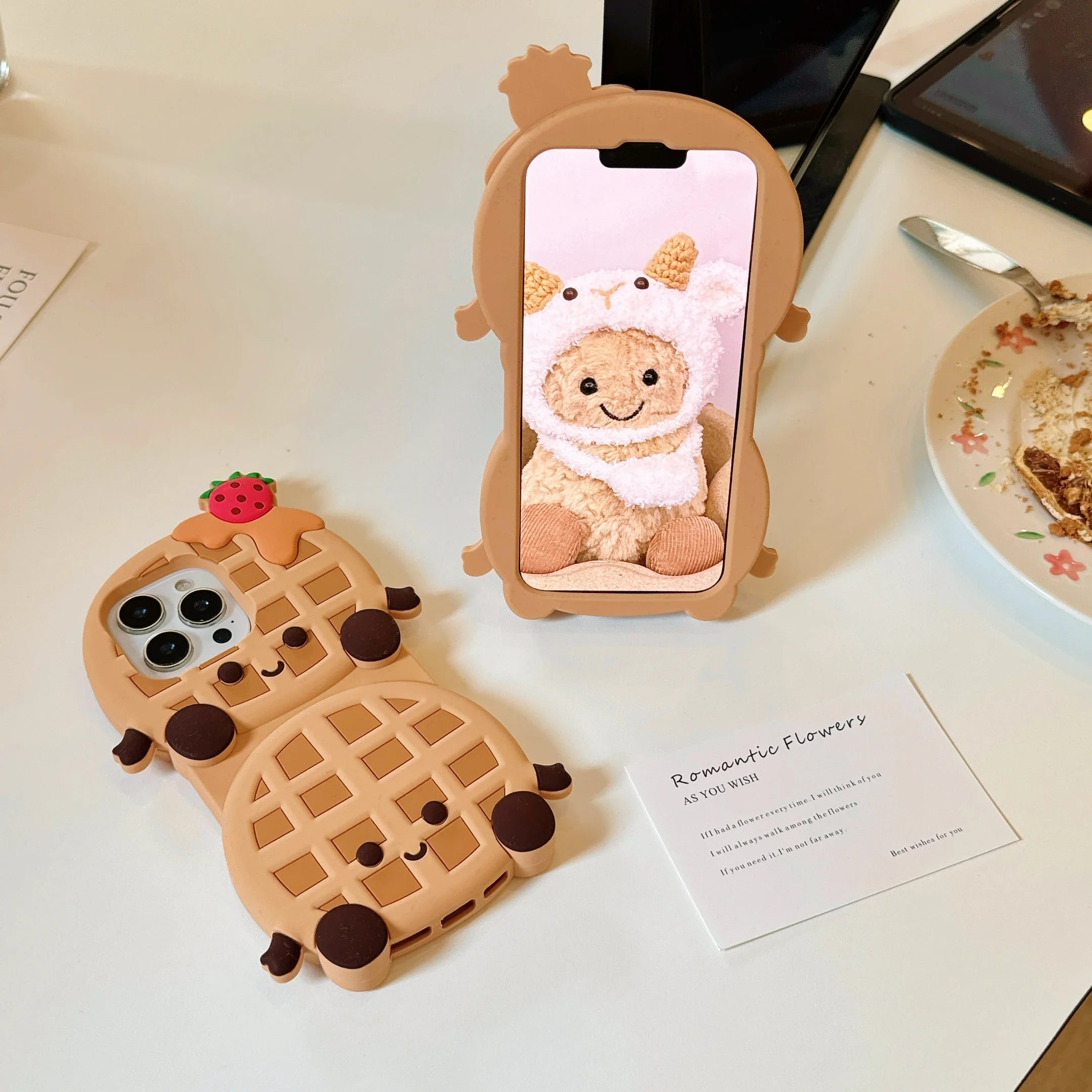 Two kawaii cute phone cases shaped like a waffle and a bear in a bear costume on a table.