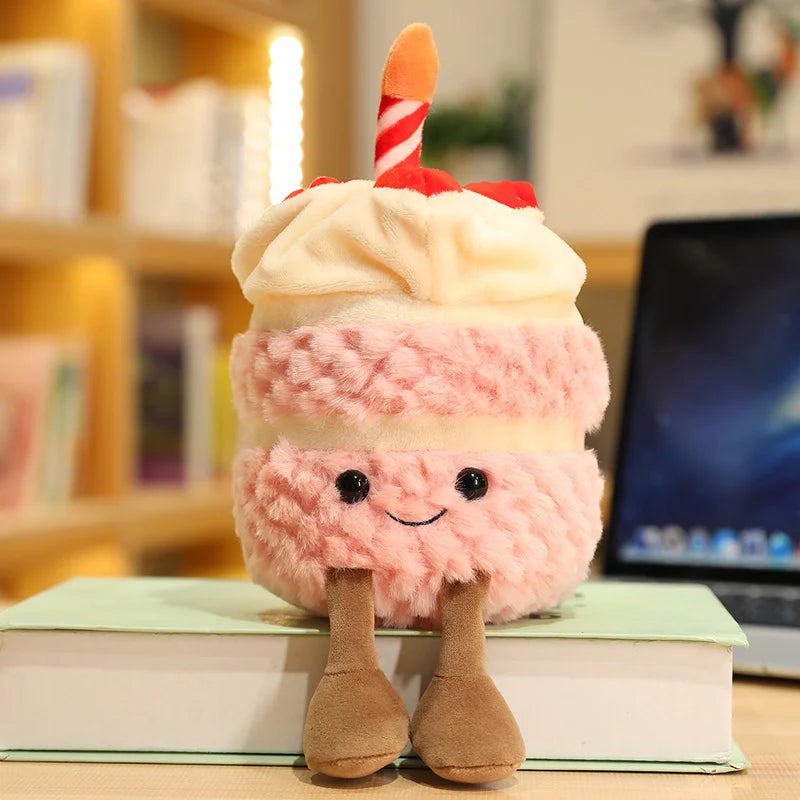 Plush kawaii toy resembling a layered dessert with a candle on a book, with a laptop and books in the background.