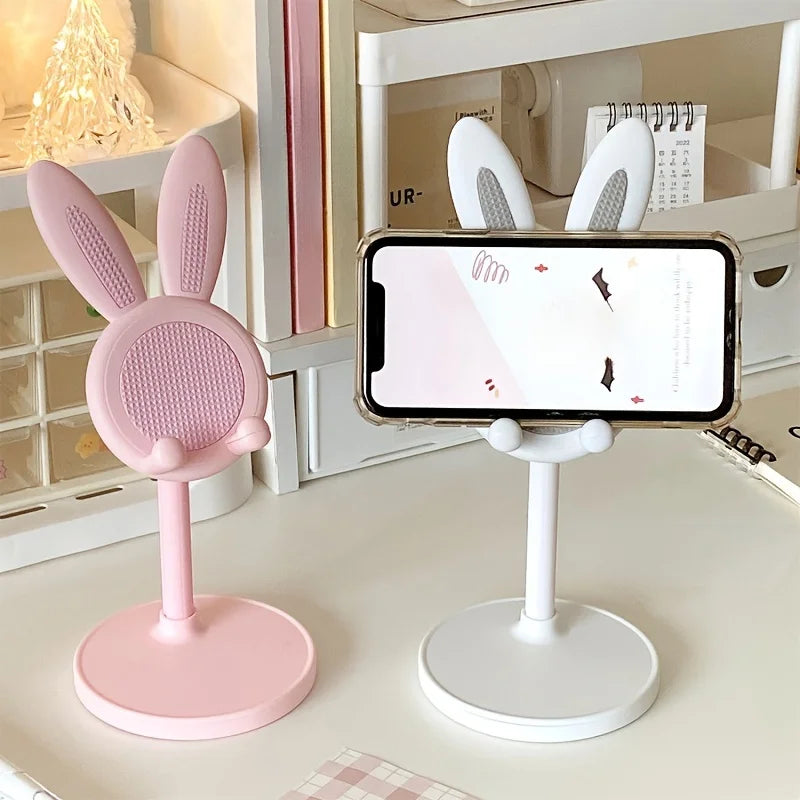 Pink bunny-shaped kawaii phone stand next to a white phone stand on a surface.