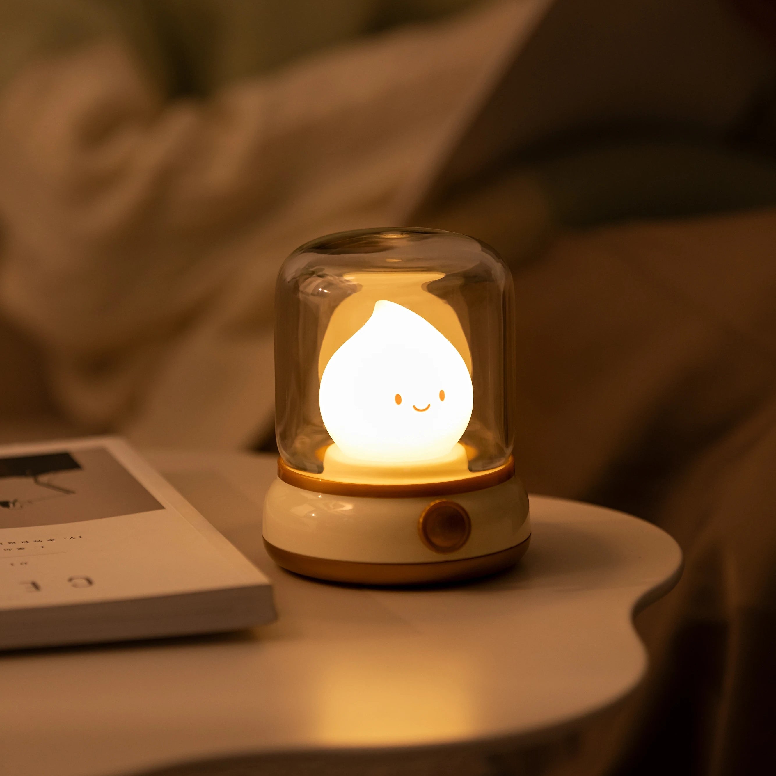 Cute night light with a kawaii smiling face on a table, with a blurred background of a person reading a book.