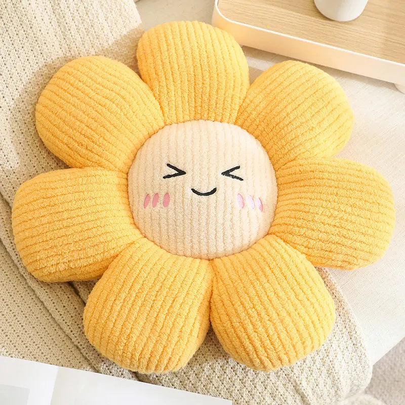 Yellow sunflower-shaped kawaii pillow with a smiling face on a beige surface.