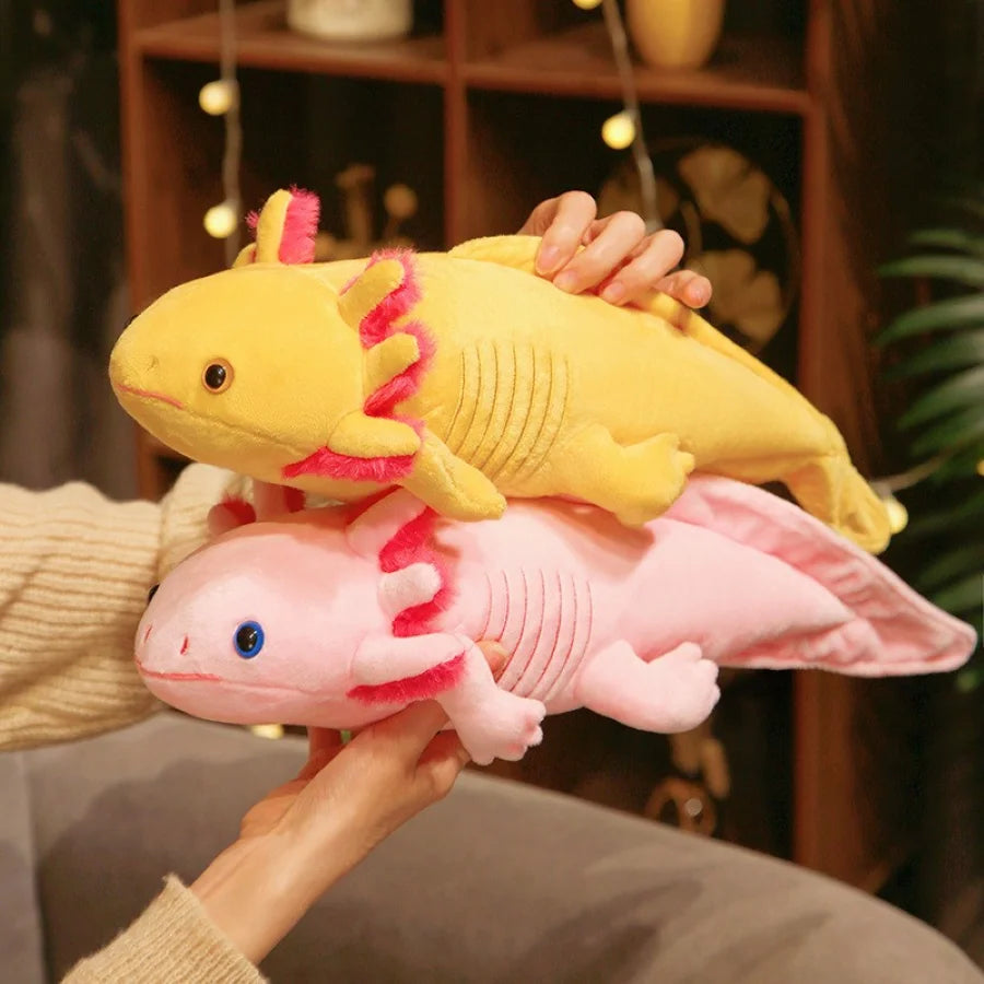 Two axolotl kawaii plush toys, one yellow and one pink, held by a person.