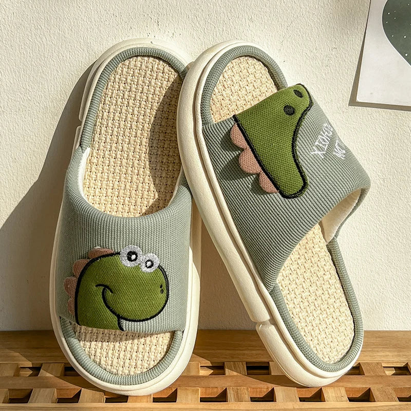Pair of light gray slippers with green frog kawaii designs on a wooden surface.
