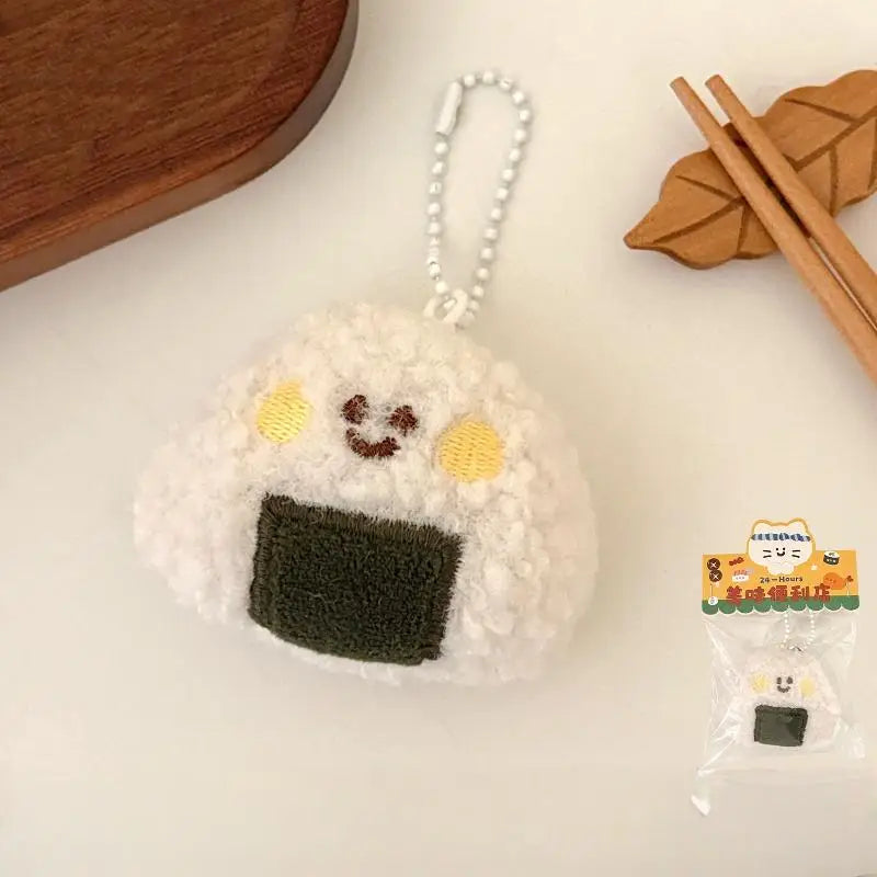 Keychain shaped like a kawaii cartoon character onigiri with a small package of onigiri in the background.