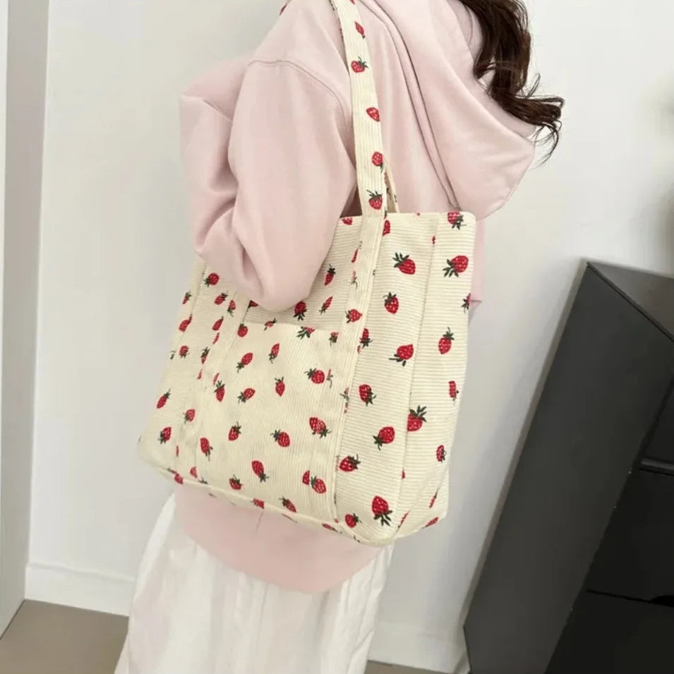 Person holding a tote bag with kawaii strawberry pattern against a neutral background