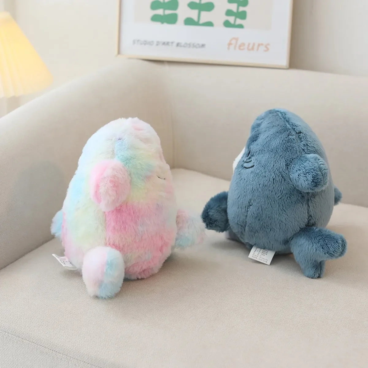Two plush kawaii toys, one multicolored and one blue, sitting on a light-colored couch.