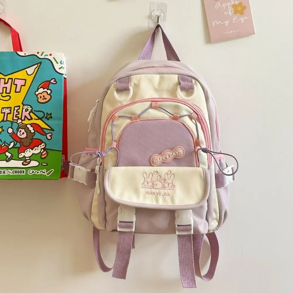Children's Kawaii backpack with pink straps hanging on a white wall next to a book.