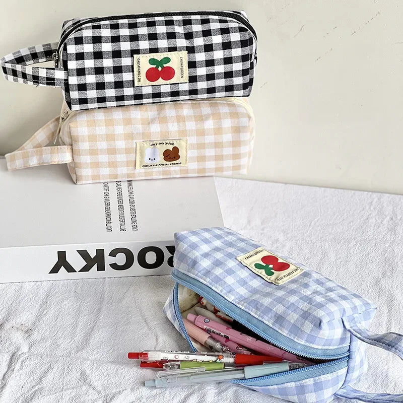 Three gingham-patterned kawaii pouches with cherry labels on a white surface.