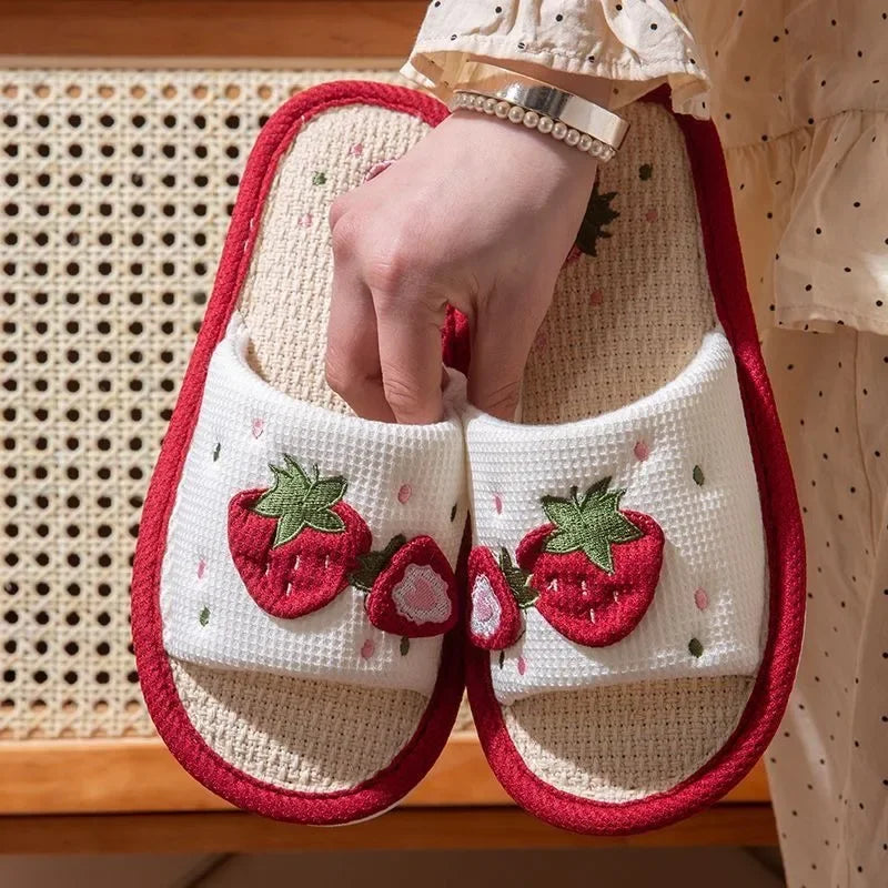 White slippers with red strawberry kawaii design held by a person against a woven background