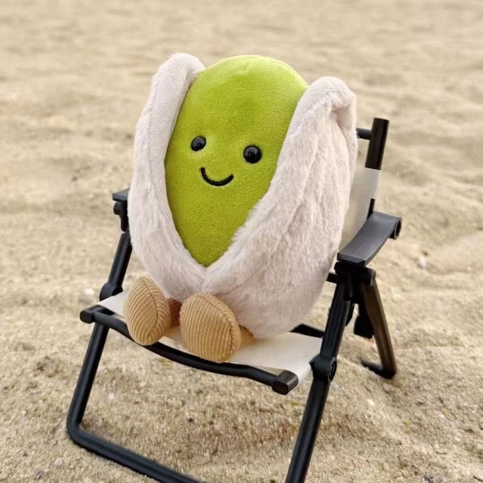 Plush kawaii toy resembling a pod with a face sitting on a small chair on sand
