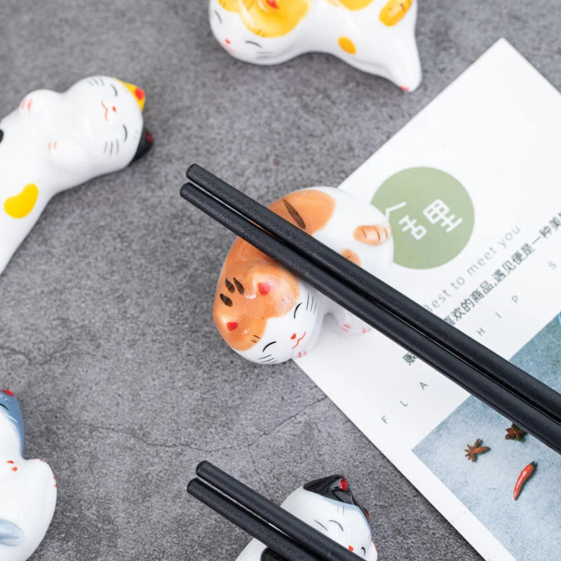 Black chopsticks on a gray surface with ceramic kawaii cat figurines and a magazine.
