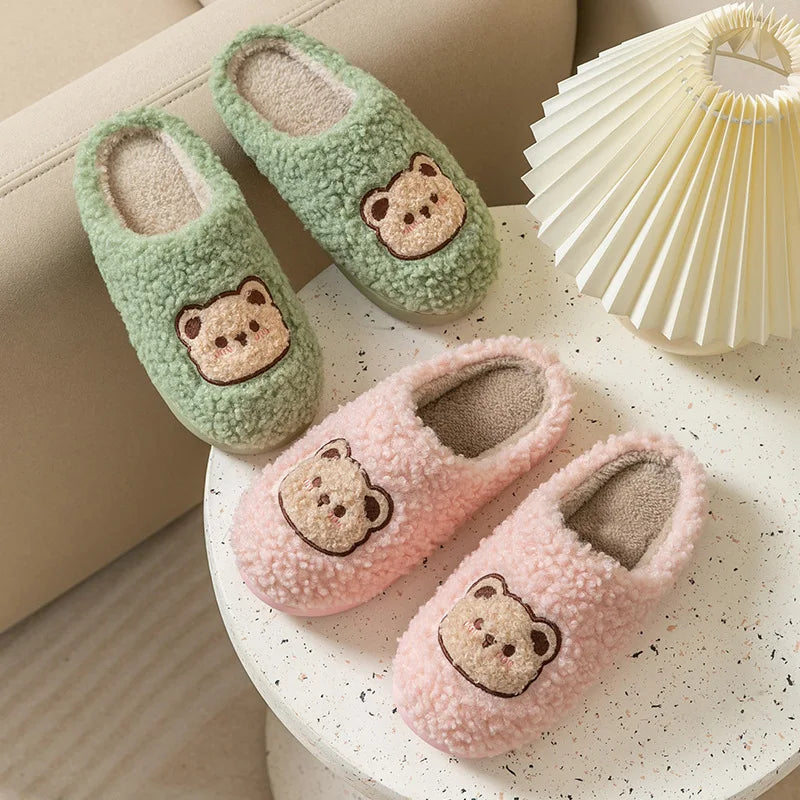 Pair of green and pink slippers with kawaii bear faces on a white surface.