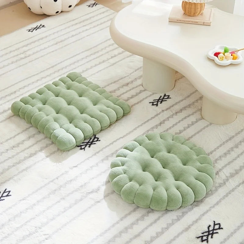 Two green textured kawaii cushions on a white floor with a light-colored table in the background.
