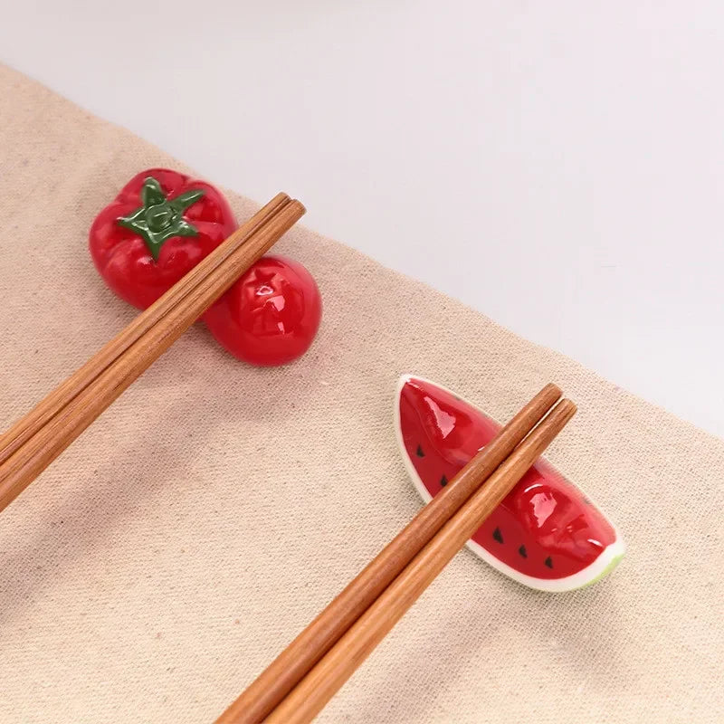 Wooden chopsticks on a beige surface with ceramic kawaii tomato and watermelon slice holders.