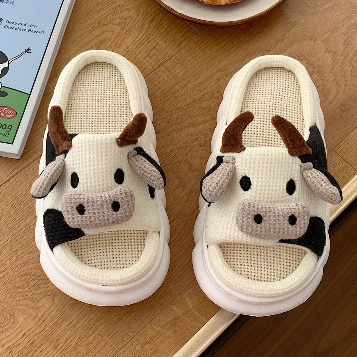 Pair of cow-themed kawaii slippers on a wooden surface