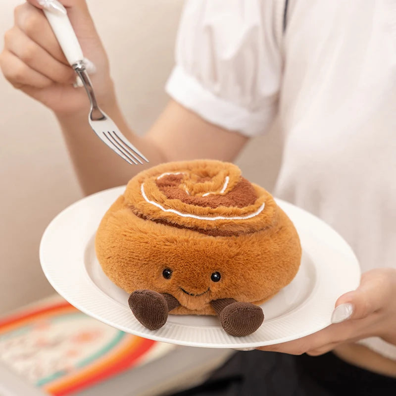 Kawaii plush cinnamon roll toy on a plate held by a person with a fork.