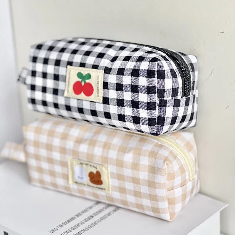Two checkered kawaii pouches stacked on a surface with visible text.