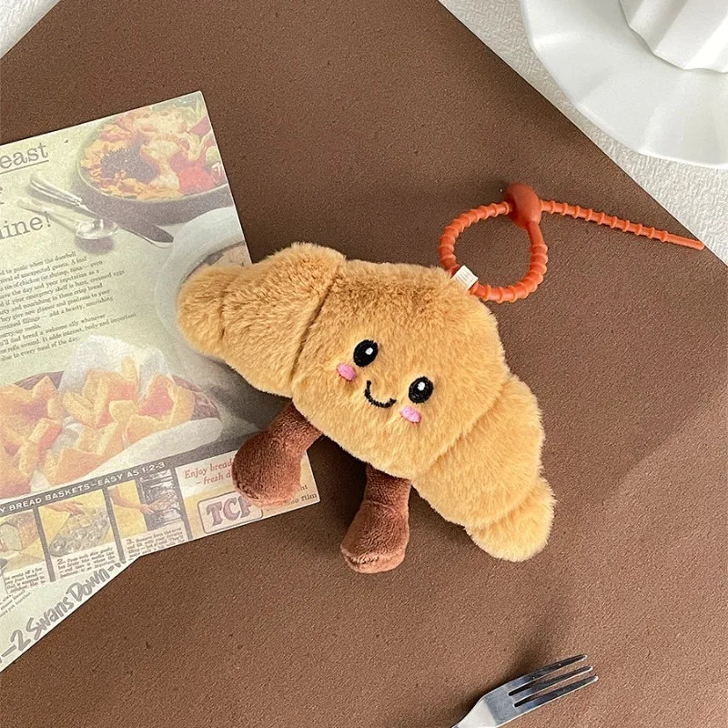 Plush kawaii toy resembling a bread roll with a smiling face on a brown surface next to a newspaper and fork.