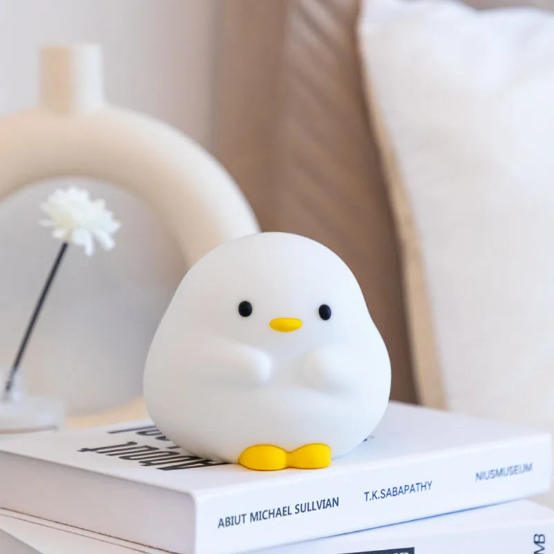 White duck-shaped kawaii night light with a yellow beak on top of books