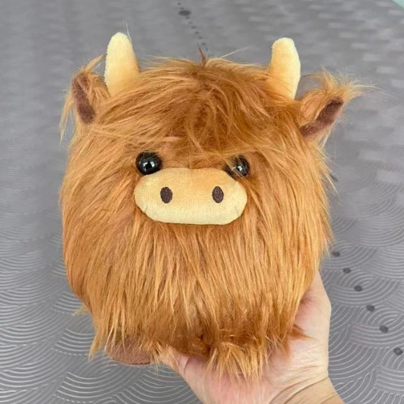 Plush kawaii toy resembling a Highland cow held by a hand against a gray background