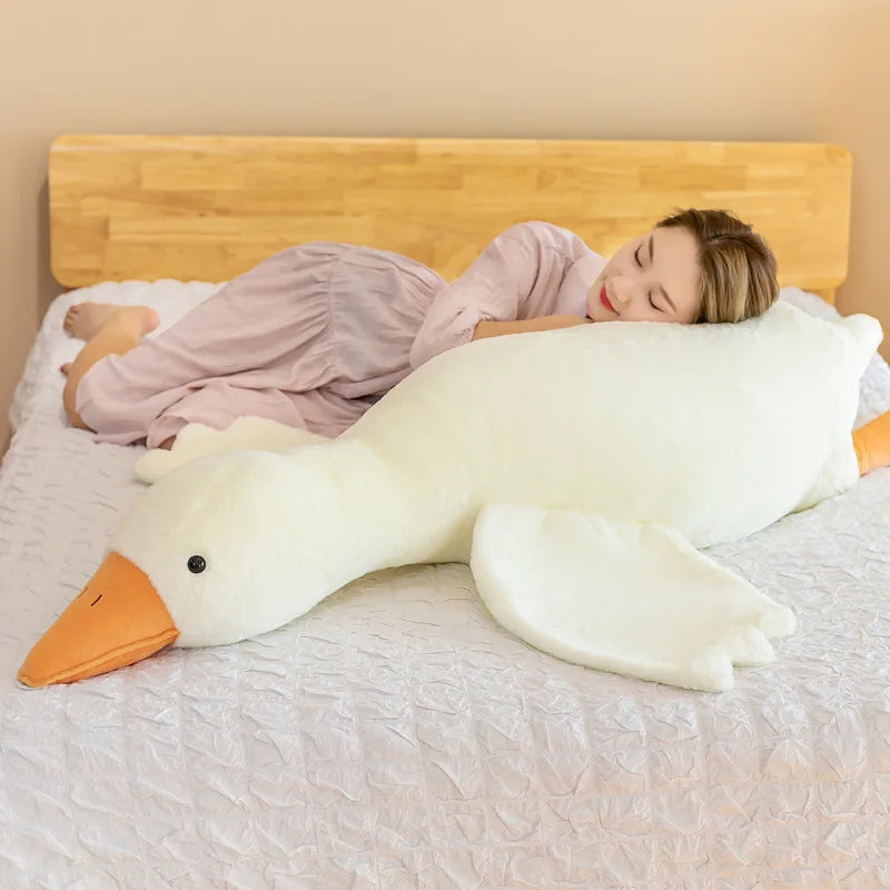 Person lying on a bed with a large duck-shaped kawaii plush pillow