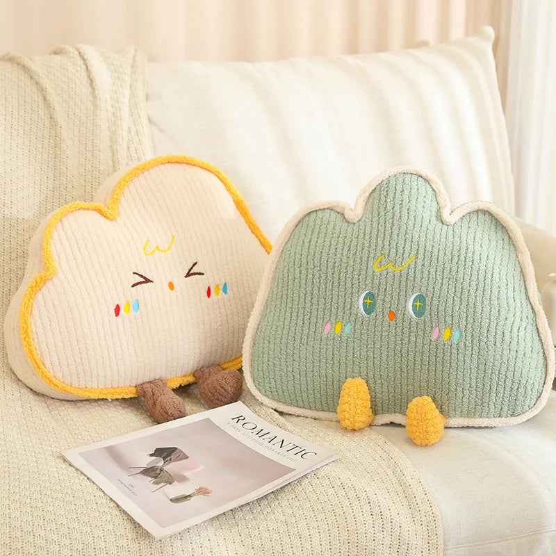 Two cloud-shaped kawaii cushions with embroidered faces on a couch next to a magazine.
