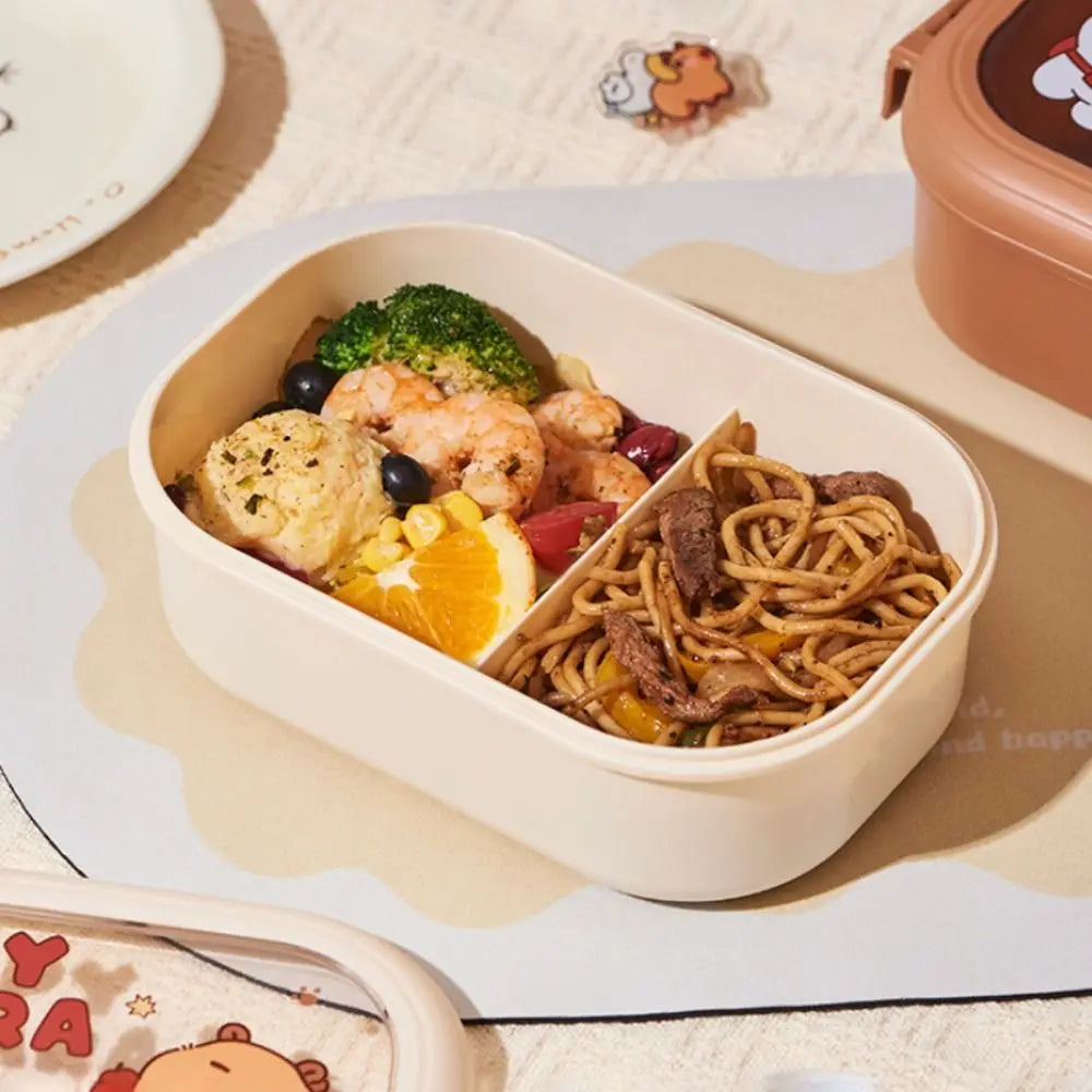 Kawaii meal container with food including noodles, vegetables, and fruits on a light surface.