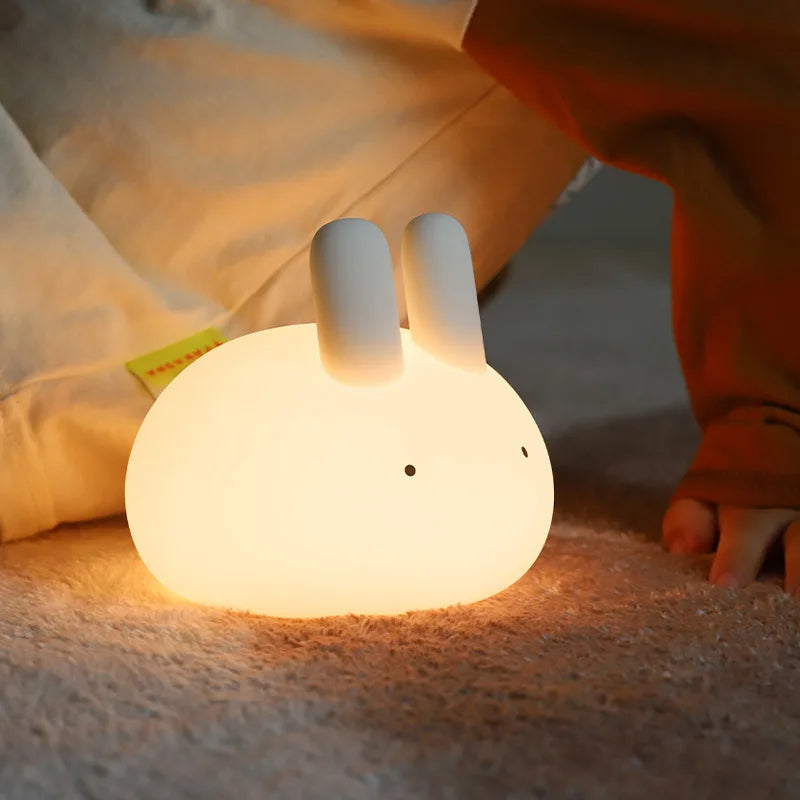 Cute rabbit-shaped kawaii night light on a soft surface with a child in the background
