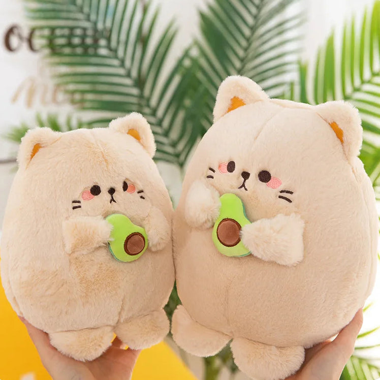 Two kawaii plush toys resembling cats holding avocados with a blurred green leafy background.