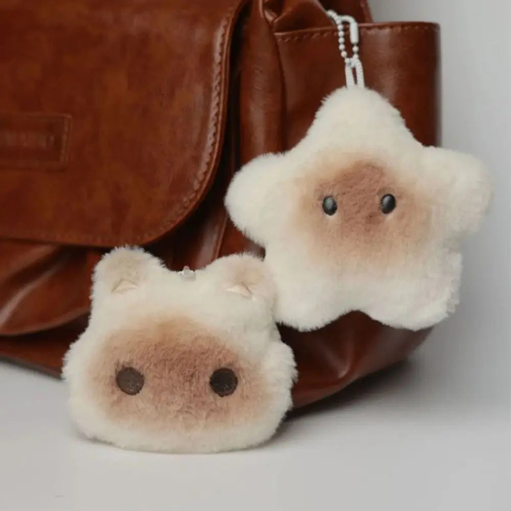 Two kawaii fluffy animal keychains hanging from a brown leather bag.
