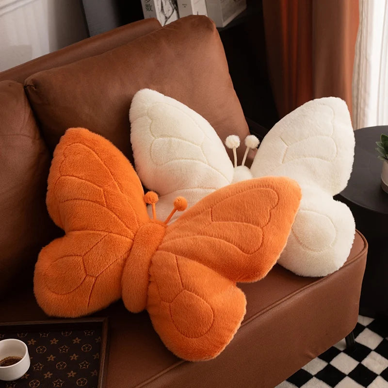 Butterfly-shaped kawaii pillow with orange wings and white body on a brown couch.
