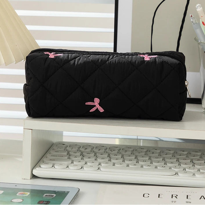 Black quilted kawaii pouch with pink accents on a desk
