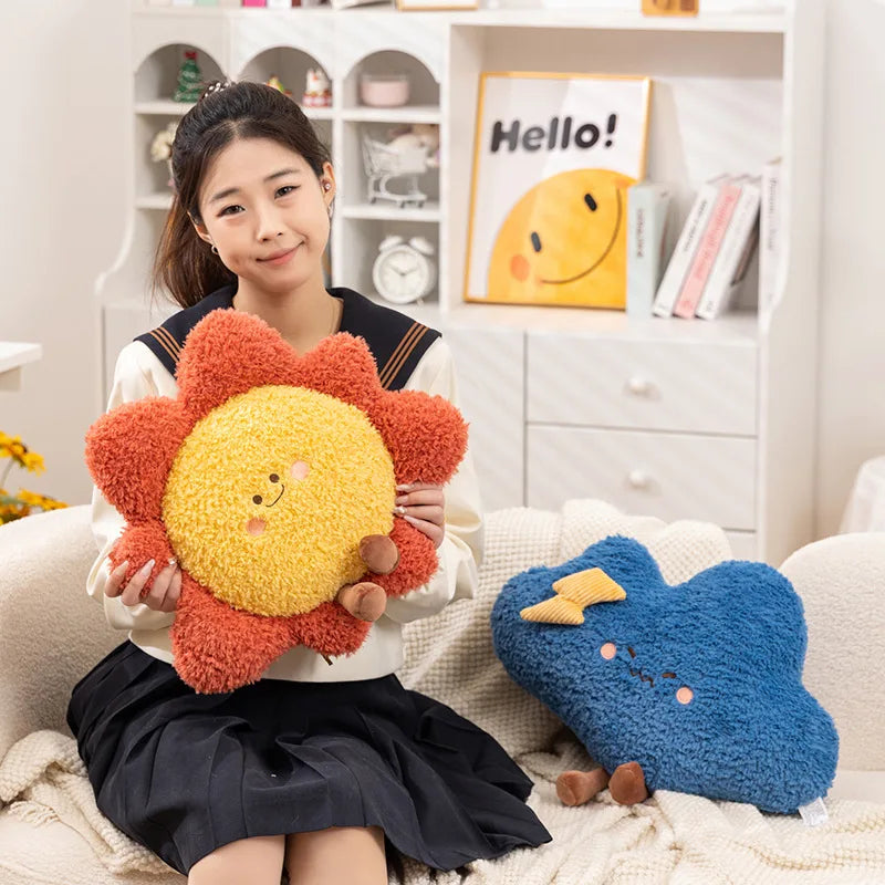 Person holding a sun-shaped kawaii plush toy with a blue plush toy on a couch in a room.