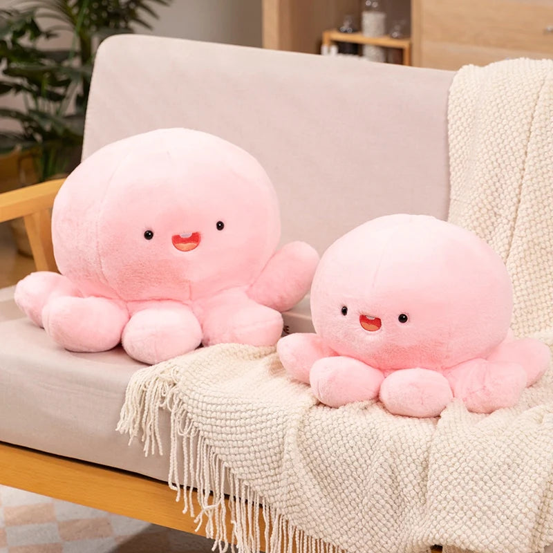 Two pink kawaii plush octopus toys on a beige couch with a blanket.