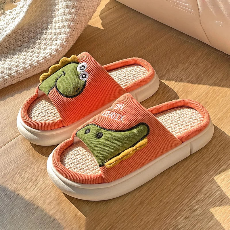 Pair of orange slippers with green kawaii dinosaur design on a wooden floor.