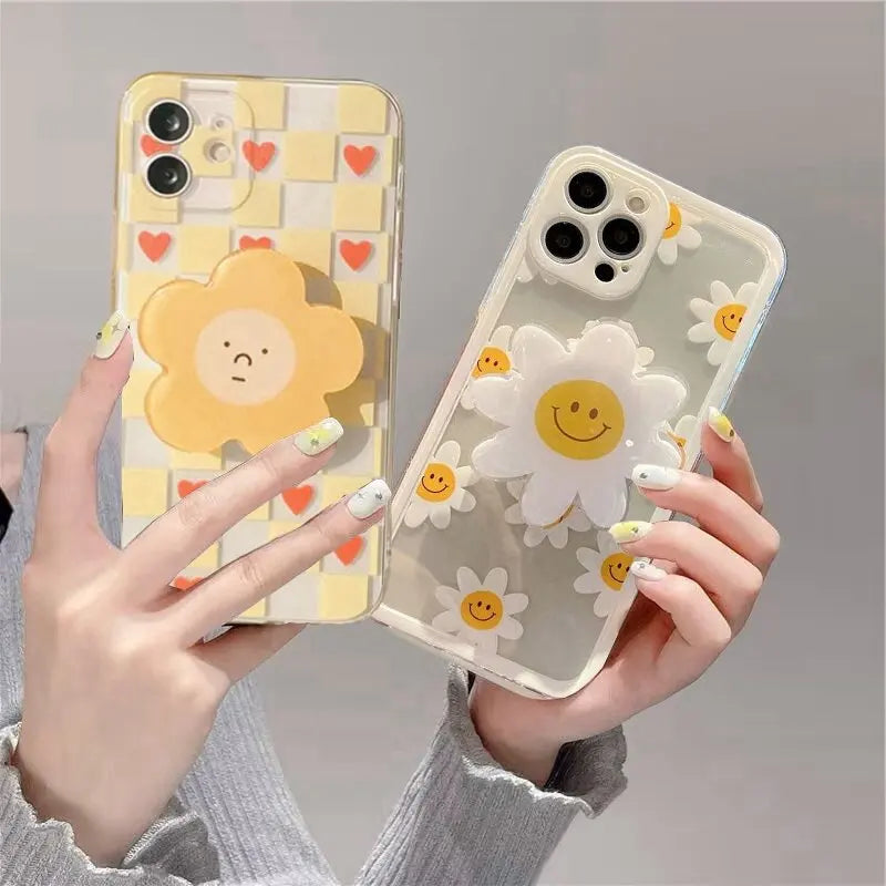 Two phone cases with kawaii cartoon flower designs held by a person against a gray background